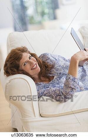 Stock Photography - Woman lying on sofa and using laptop. Fotosearch