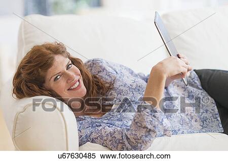 Stock Photography - Woman lying on sofa and using laptop. Fotosearch