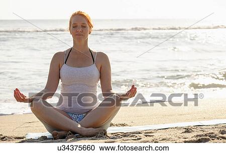 Stock Image - Woman practicing yoga on beach. Fotosearch