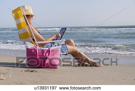 Woman sitting on deckchair and using laptop View Large Photo Image Stock Photo - Woman sitting on deckchair and using laptop. Fotosearch