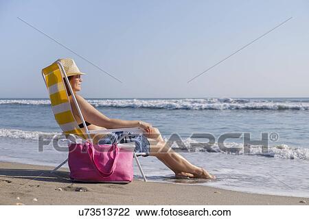 Woman sitting on deckchair on beach View Large Photo Image Stock Image - Woman sitting on deckchair on beach. Fotosearch