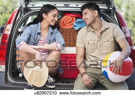Stock Image - Young couple sitting in open car trunk. Fotosearch