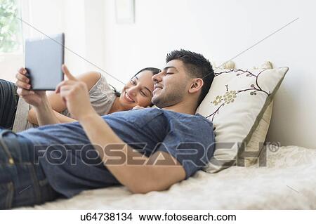 Young couple using digital tablet in bed View Large Photo Image Picture - Young couple using digital tablet in bed. Fotosearch