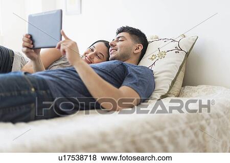 Young couple using digital tablet in bed View Large Photo Image Stock Photo - Young couple using digital tablet in bed. Fotosearch