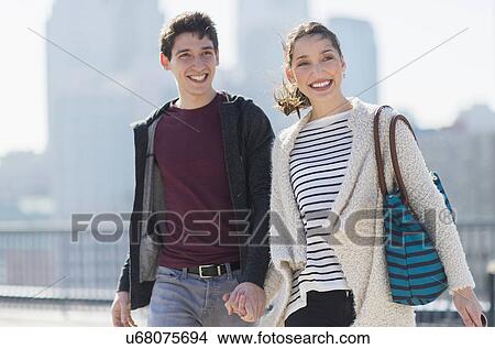 Young couple walking, buildings in background View Large Photo Image Picture - Young couple walking, buildings in background. Fotosearch