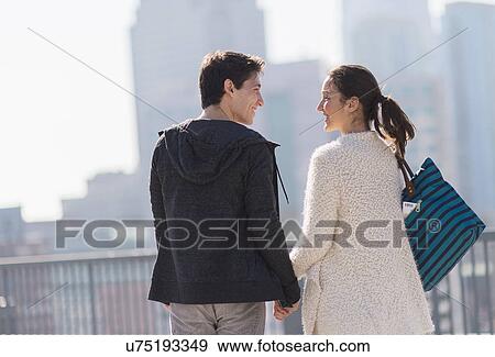 Stock Photo - Young couple walking, buildings in background. Fotosearch