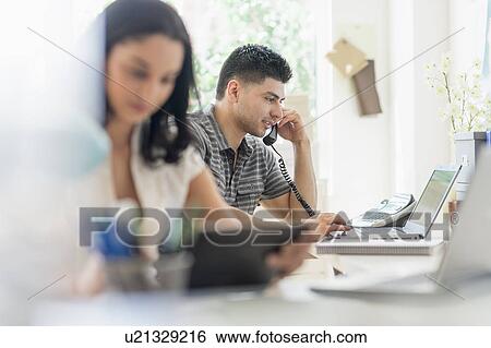 Stock Photograph - Young man and woman working in office. Fotosearch