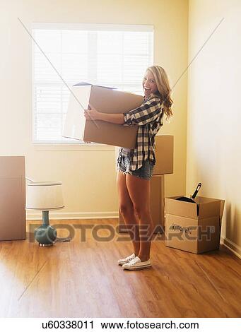 Stock Image - Young woman carrying box in her new house. Fotosearch