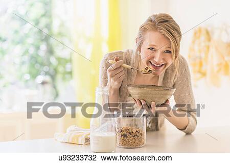 Stock Image - Young woman eating granola for breakfast. Fotosearch