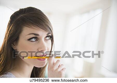 Young woman holding pencil in her mouth View Large Photo Image Stock Photograph - Young woman holding pencil in her mouth. Fotosearch