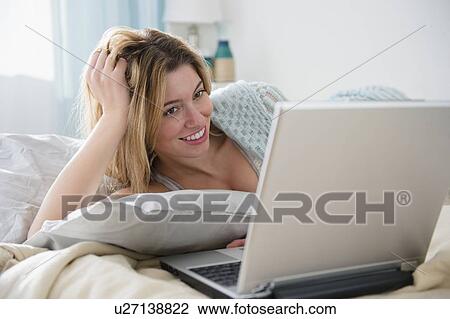 Young woman lying in bed and using laptop View Large Photo Image Stock Image - Young woman lying in bed and using laptop. Fotosearch