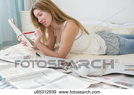 Stock Photo - Young woman lying on bed and doing job search. Fotosearch
