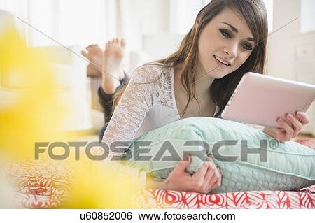 Young woman lying on bed with digital tablet View Large Photo Image Stock Photograph - Young woman lying on bed with digital tablet. Fotosearch