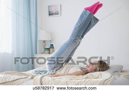 Stock Photo - Young woman lying on bed with legs up. Fotosearch