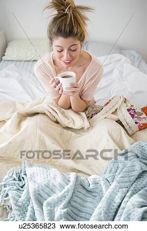 Young woman sitting in bed with coffee View Large Photo Image Stock Image - Young woman sitting in bed with coffee. Fotosearch