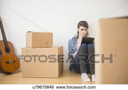 Stock Photo - Young woman sitting on floor with digital tablet with boxes around her. Fotosearch
