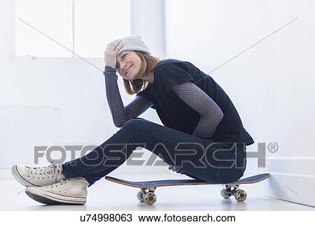 Stock Image - Young woman sitting on skateboard. Fotosearch