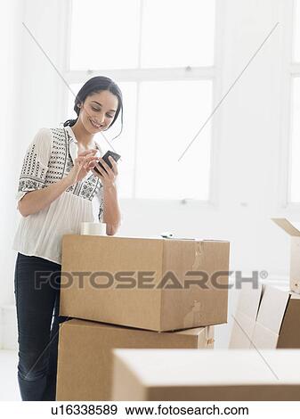 Young woman standing among boxes in new home and using mobile phone View Large Photo Image Stock Photo - Young woman standing among boxes in new home and using mobile phone. Fotosearch