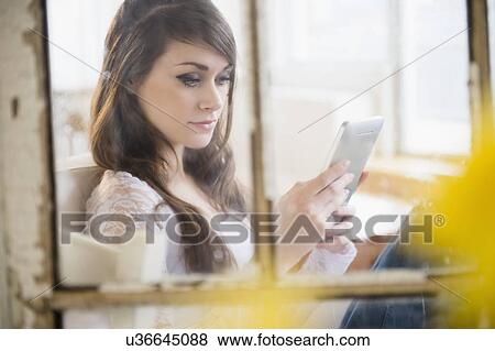 Stock Photo - Young woman using digital tablet in living room. Fotosearch