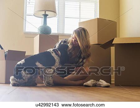 Stock Image - Young woman with dog in their new house. Fotosearch