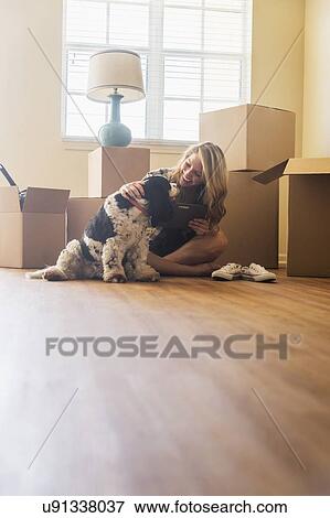 Stock Photo - Young woman with dog in their new house. Fotosearch