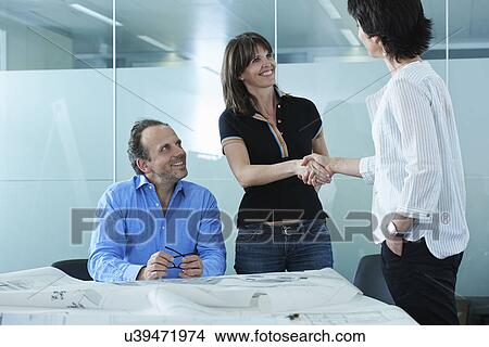 Architect greeting client with blueprints on boardroom table View Large Photo Image Picture - Architect greeting client with blueprints on boardroom table. Fotosearch