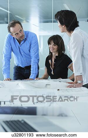 Stock Image - Architect showing client blueprints on boardroom table. Fotosearch