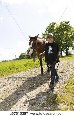 Boy leading horse along dirt track View Large Photo Image Stock Photo - Boy leading horse along dirt track. Fotosearch