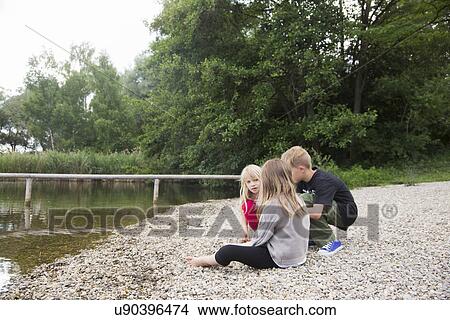 Brother and two sisters sitting chatting on lakeside View Large Photo Image Picture - Brother and two sisters sitting chatting on lakeside. Fotosearch
