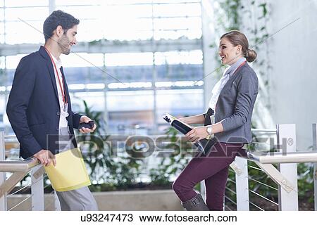 Stock Image - Businessman and businesswoman chatting in conference centre atrium. Fotosearch