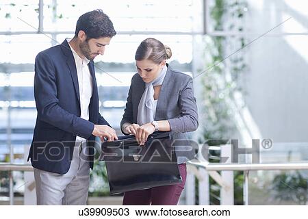 Stock Image - Businessman and businesswoman opening briefcase in conference centre atrium. Fotosearch