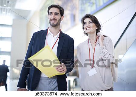 Picture - Businessman and businesswoman with paperwork in conference centre atrium. Fotosearch