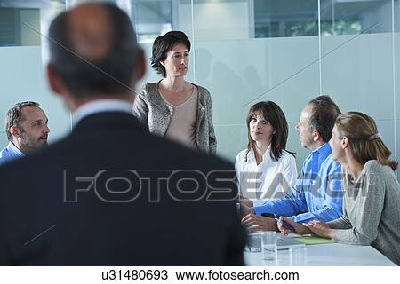 Stock Image - Businessmen and women arguing around boardroom table. Fotosearch