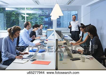 Picture - Businesspeople sitting on opposite sides of screen partition, working. Fotosearch