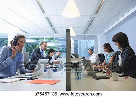 Stock Photography - Businesspeople sitting on opposite sides of screen partition, working. Fotosearch