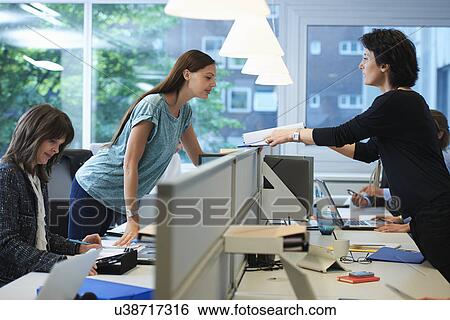 Stock Photograph - Businesswoman passing paperwork across screen partition in office. Fotosearch