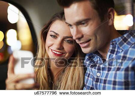 Couple looking at smartphone city taxi at night View Large Photo Image Stock Photograph - Couple looking at smartphone city taxi at night. Fotosearch