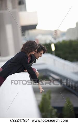 Couple looking down and pointing from city rooftop View Large Photo Image Picture - Couple looking down and pointing from city rooftop. Fotosearch