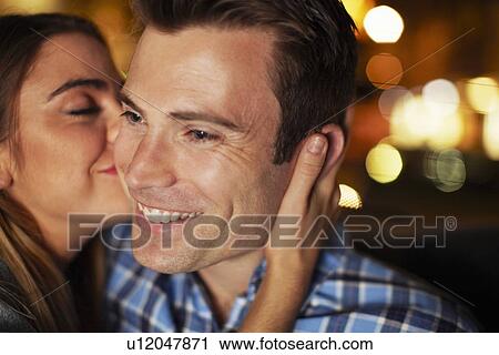 Stock Image - Couple sharing kiss on the cheek in city taxi at night. Fotosearch