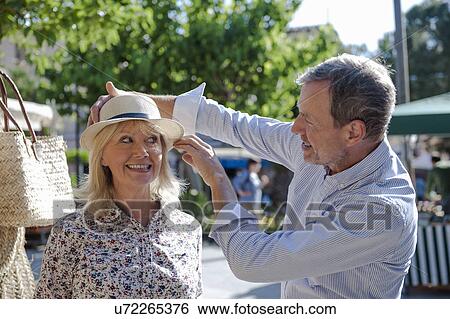 Stock Photograph - Couple trying on hat at market, Mallorca, Spain. Fotosearch