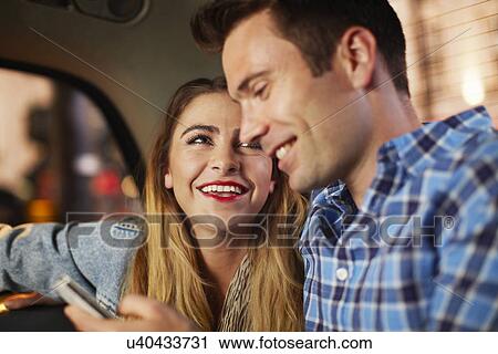 Stock Image - Couple with smartphone city taxi at night. Fotosearch