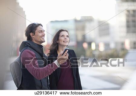 Couple with smartphone looking up on city street View Large Photo Image Stock Photo - Couple with smartphone looking up on city street. Fotosearch