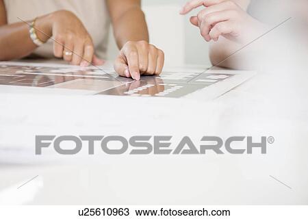 Stock Image - Cropped shot of two businesswomen's hands and blueprint. Fotosearch