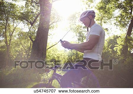 Cyclist using smartphone in forest View Large Photo Image Stock Photo - Cyclist using smartphone in forest. Fotosearch