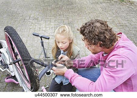 Stock Photo - Father and daughter mending bike. Fotosearch