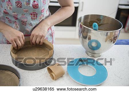 Stock Photography - Female hands lining cake tins with greaseproof paper in bakery. Fotosearch