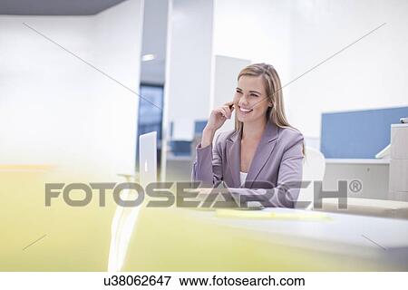 Stock Photo - Female office worker at desk, smiling. Fotosearch