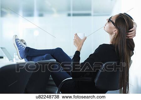 Stock Photo - Female office worker leaning back with feet up on conference table. Fotosearch