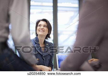 Stock Image - Female office worker looking up, smiling. Fotosearch
