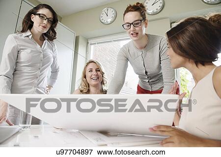 Stock Photo - Four businesswomen looking at blueprint in office. Fotosearch